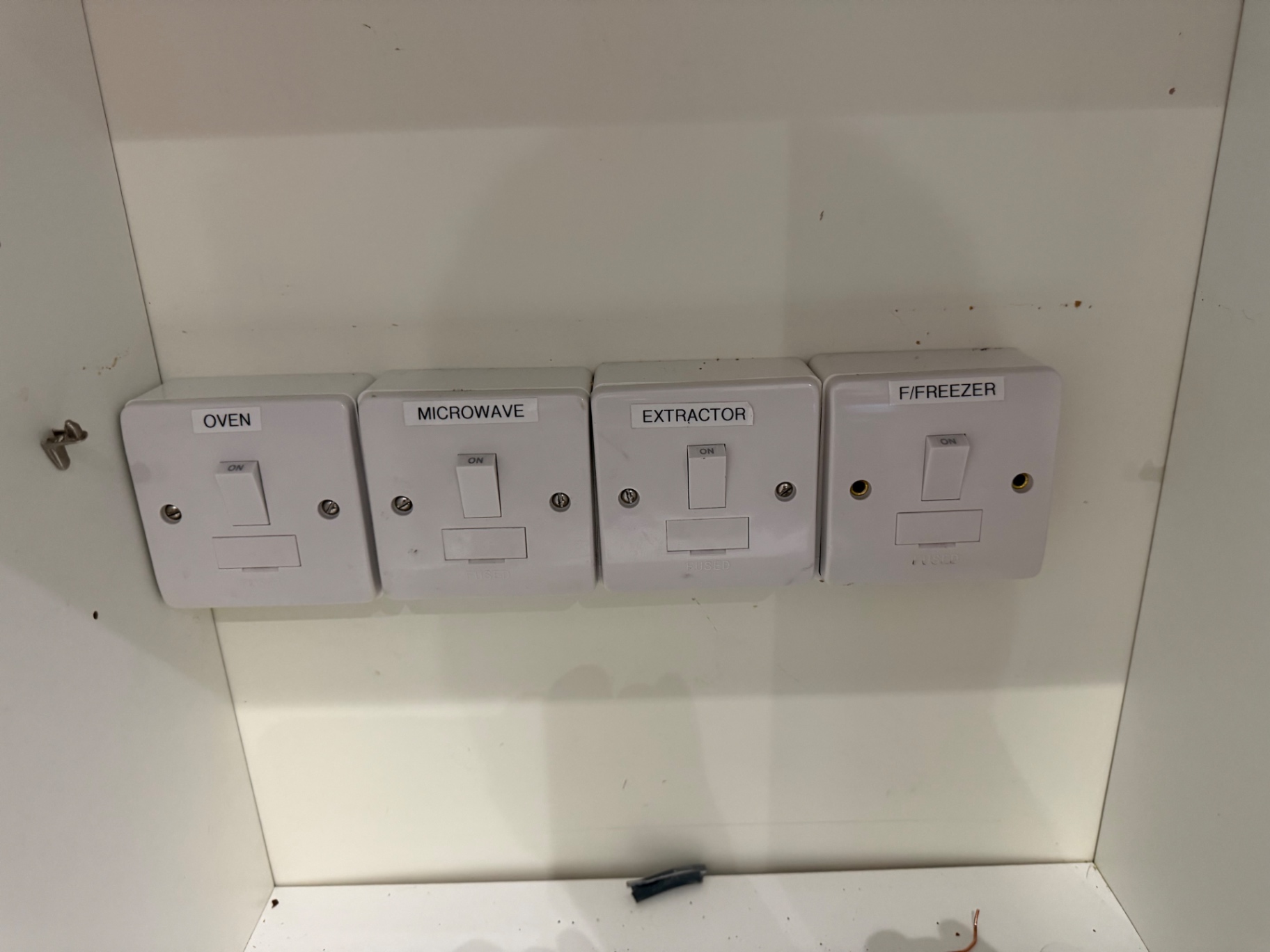 The bank of four labelled 13A switched fused spurs — Oven, Microwave, Extractor and F/Freezer — feeding kitchen appliances before removal.