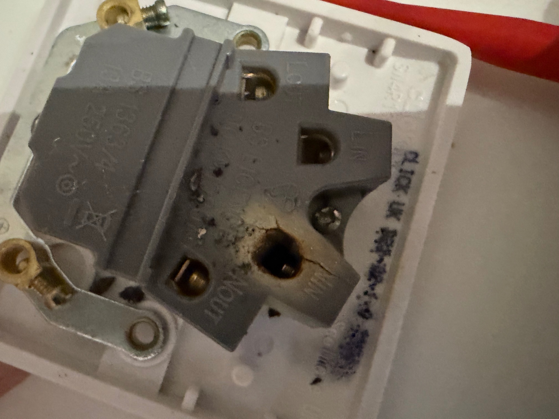 Backplate of the failed 13A fused spur — cracked housing and burnt residue around the neutral terminal from long-term arcing.